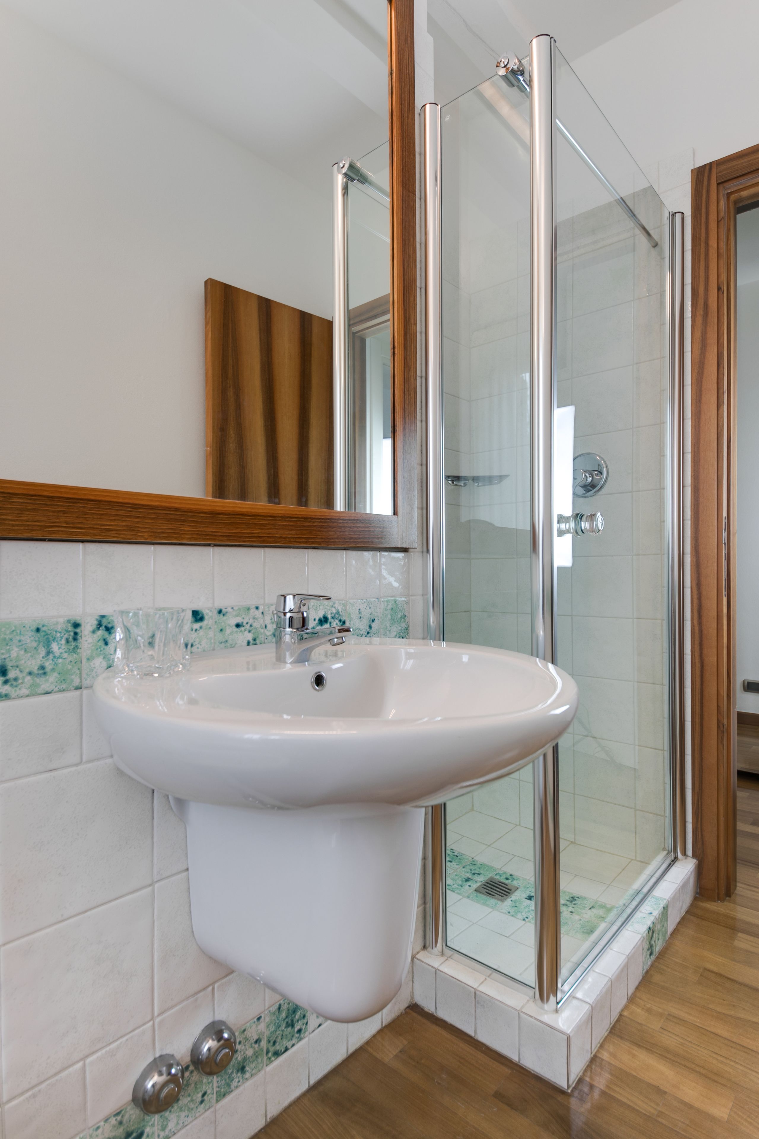 A bathroom with a white sink, a glass shower enclosure, and a wooden-framed mirror.