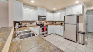 A kitchen with white cabinets, stainless steel appliances, and a tiled floor. - Spark Getaways: The Shapiro (Lubbock)