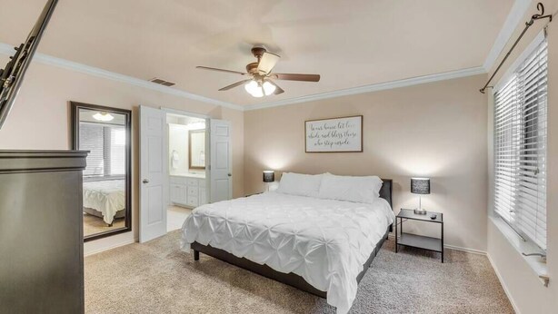 A bedroom with a bed, bedside tables, a ceiling fan, a door, and a window with blinds. - Spark Getaways: The Shapiro (Lubbock)