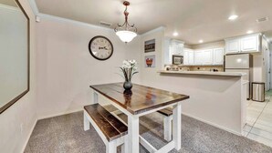 A kitchen with white cabinets, a wooden dining table, and a clock on the wall. - Spark Getaways: The Shapiro (Lubbock)