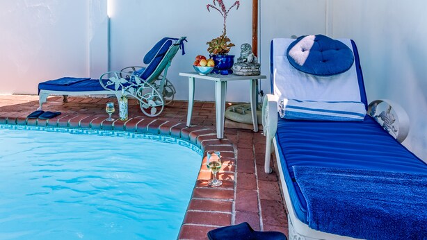A poolside area with a bed, a chair, and a table with a plant and fruit bowl. - Bleu Cobalt Cottage (Franschhoek)