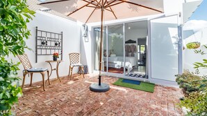 A patio with a brick floor, a table, two chairs, and a large umbrella. - Bleu Cobalt Cottage (Franschhoek)