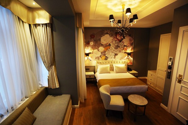 A hotel room with a bed, a sofa, a chair, a small table, a chandelier, and a floral wall mural. - Royal Tophane (Istanbul)