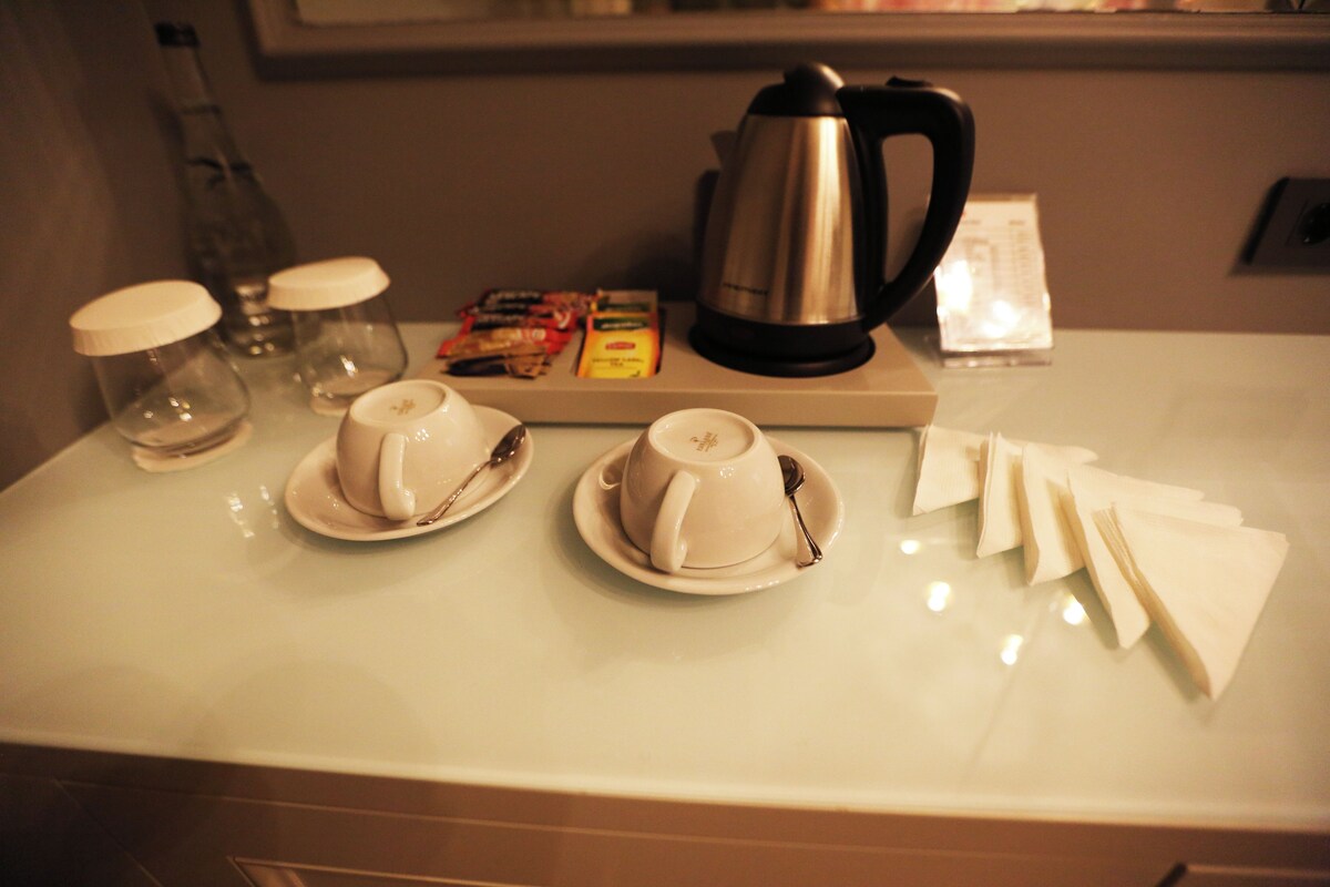 A kitchen counter with two cups, a coffee pot, and some condiments.