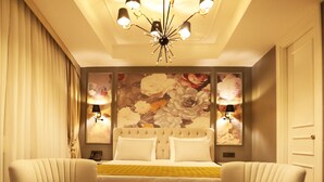 Une chambre d’hôtel comprenant un lit, deux fauteuils, une petite table, un lustre et des lampes fixées au mur.