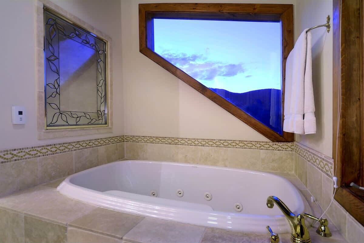 A bathroom with a large bathtub, a window with a view, and a decorative mirror.