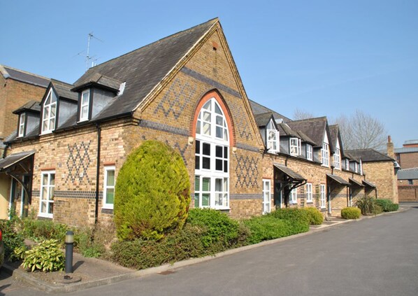 Traditional brick building with a central entrance and arched window, set amidst a well-manicured hedge and paved driveway.