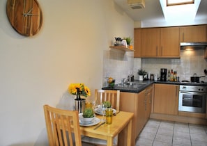 Compact kitchen with a dining area, featuring a stainless steel oven, sink, and small dining table with a chair.