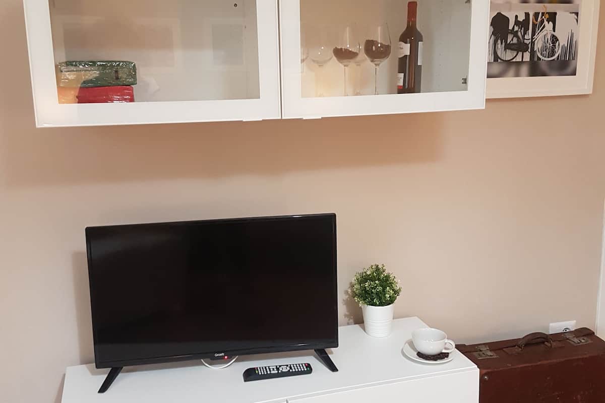 A white entertainment unit with a flat-screen TV, a remote control, a small potted plant, and a white cup on a saucer.