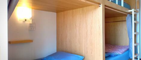 A bunk bed room with a wooden ceiling, a wall-mounted light, and a small shelf.