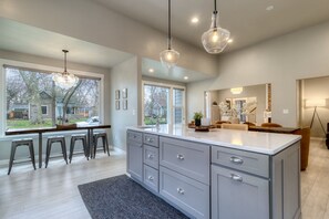 A modern kitchen with a large island, bar stools, pendant lights, and a view of the backyard.