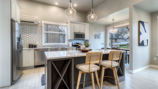 Una cucina moderna con isola centrale, sgabelli da bar, illuminazione a sospensione e vista sull'esterno.