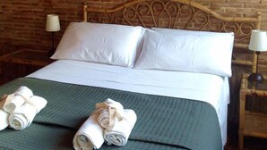 Habitación de hotel con pared de ladrillo, estructura de cama de madera, ropa de cama blanca y dos toallas enrolladas sobre la cama.