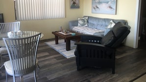 Een woonkamer met een bank, een salontafel en een eethoek met stoelen.