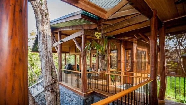 A wooden deck with a railing, surrounded by trees. - 2 Bedroom Hand Crafted Luxury Home with Jacuzzi & Fireplace (Volcano)