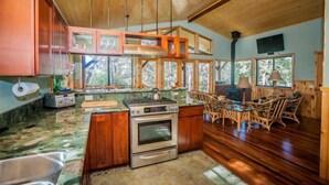 A kitchen with wooden cabinets, a stove, and a dining area with wicker chairs. - 2 Bedroom Hand Crafted Luxury Home with Jacuzzi & Fireplace (Volcano)