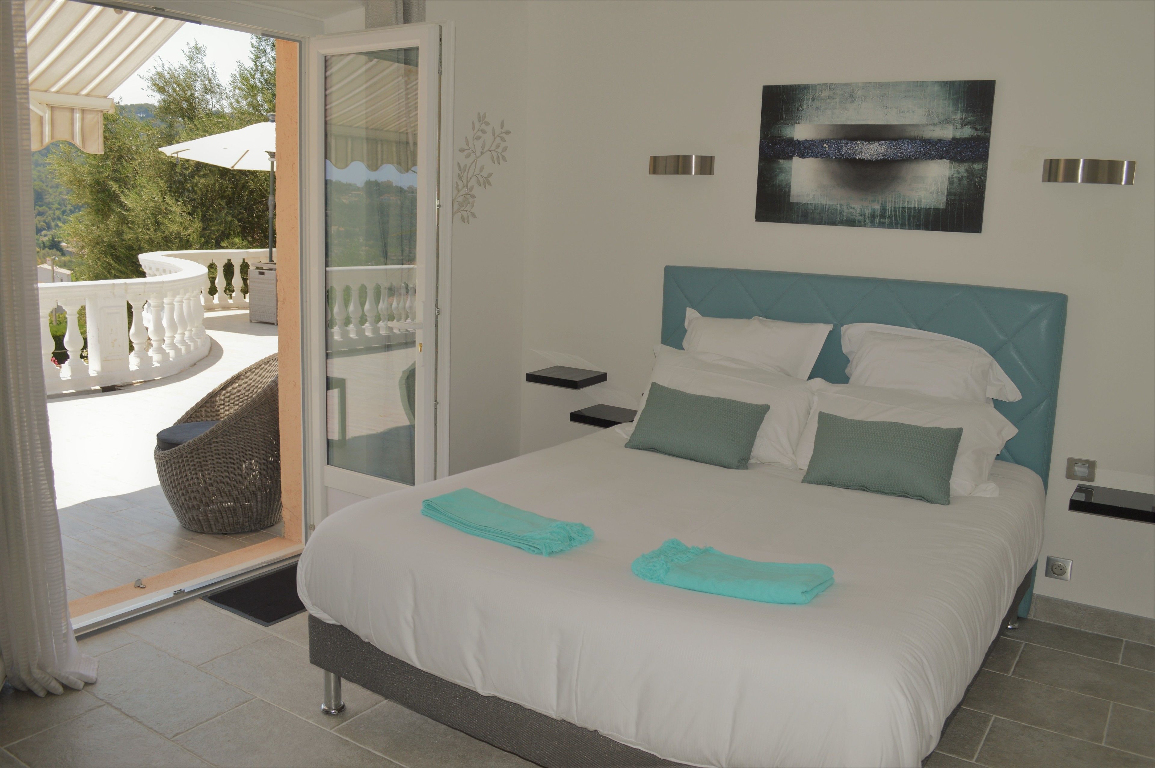 A bedroom with a bed, a nightstand, a wall-mounted light, and a view of the outdoors.