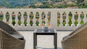Een balkon met rieten stoelen, een tafel en twee glazen drinken.