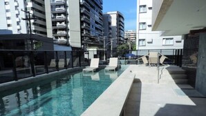 Una piscina con sillas de descanso y un cerramiento de vidrio.