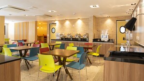 Un café moderno con mesas de madera y sillas coloridas, un muro de ladrillo y una máquina de café.