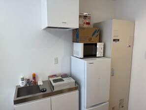 Una cocina compacta con un microondas sobre un refrigerador, un lavamanos con grifo y un gabinete debajo.