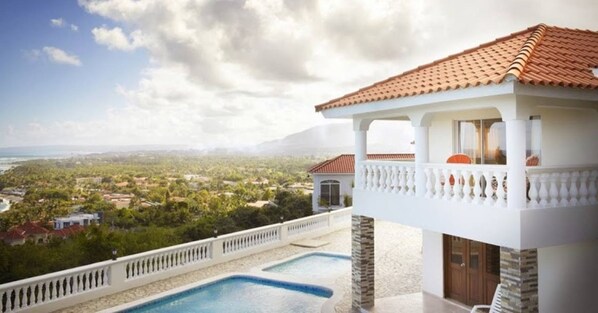A luxurious villa with a pool, white columns, and a view of a coastal landscape.