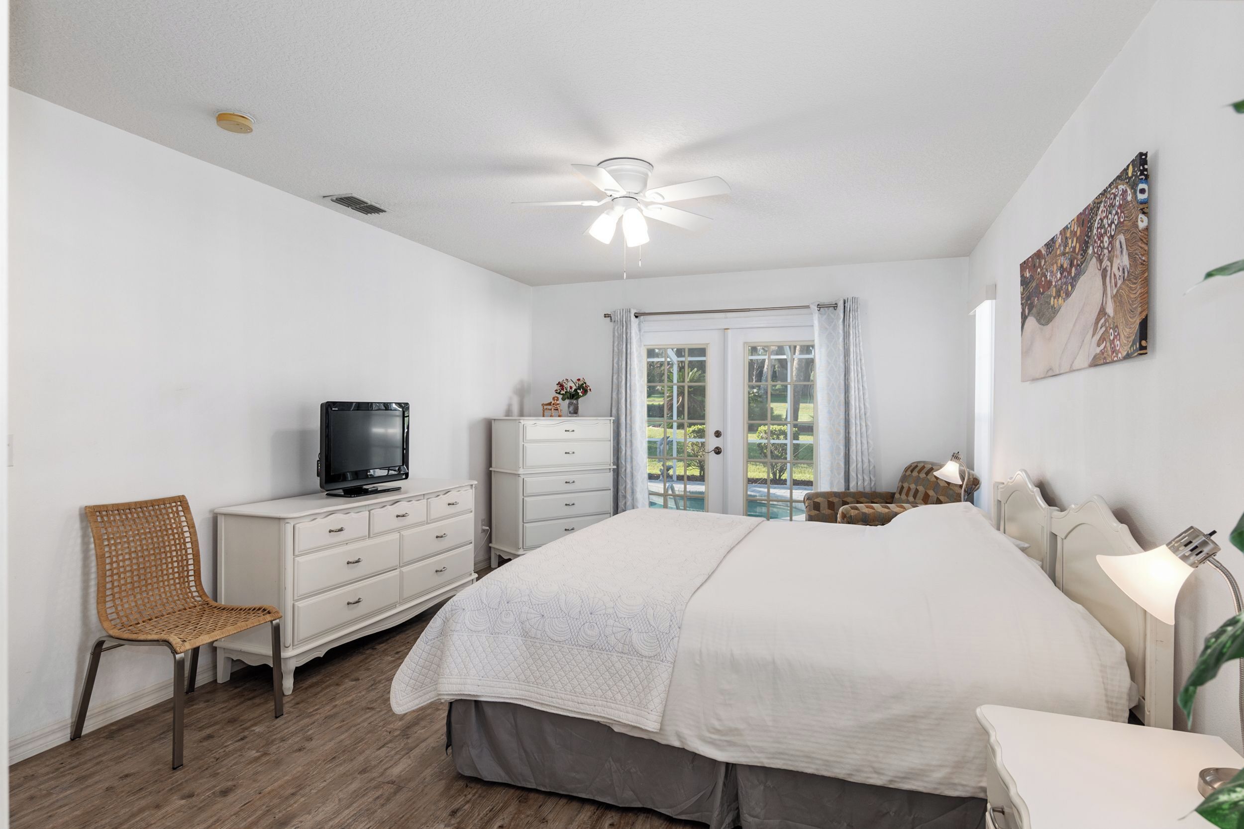 A bedroom with a bed, a television, a dresser, a chair, and a window with curtains.