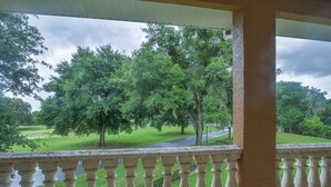 Blick von einem Balkon mit Geländer auf eine grüne Landschaft mit Bäumen und einer Straße.