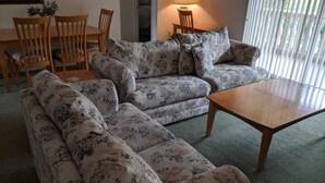 Ein Wohnzimmer mit floralen Sofas, einem Holztisch und einem Essbereich mit Holzkästen und einem Tisch.