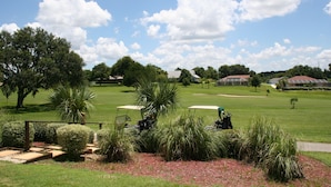 Un campo de golf con club house, césped bien cuidado y palmeras.