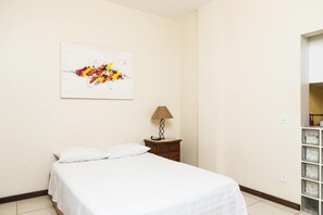 A hotel room with a bed, a nightstand with a lamp, and a wall-mounted artwork. - Studio Djalma Ulrich 49 - 100B Apartment 1 (Rio de Janeiro)