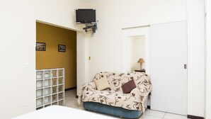 Un dormitorio con cama, sofá, televisor montado en la pared y una puerta.