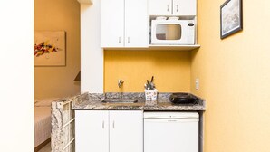 Una cocina compacta con armarios blancos, microondas, lavaplatos y un fregadero. Hay un cuadro enmarcado en la pared y un colorido cuadro abstracto en la pared contigua.