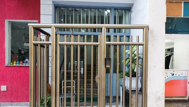 Una entrada cerrada con un portón metálico, una escalera y una planta en maceta.