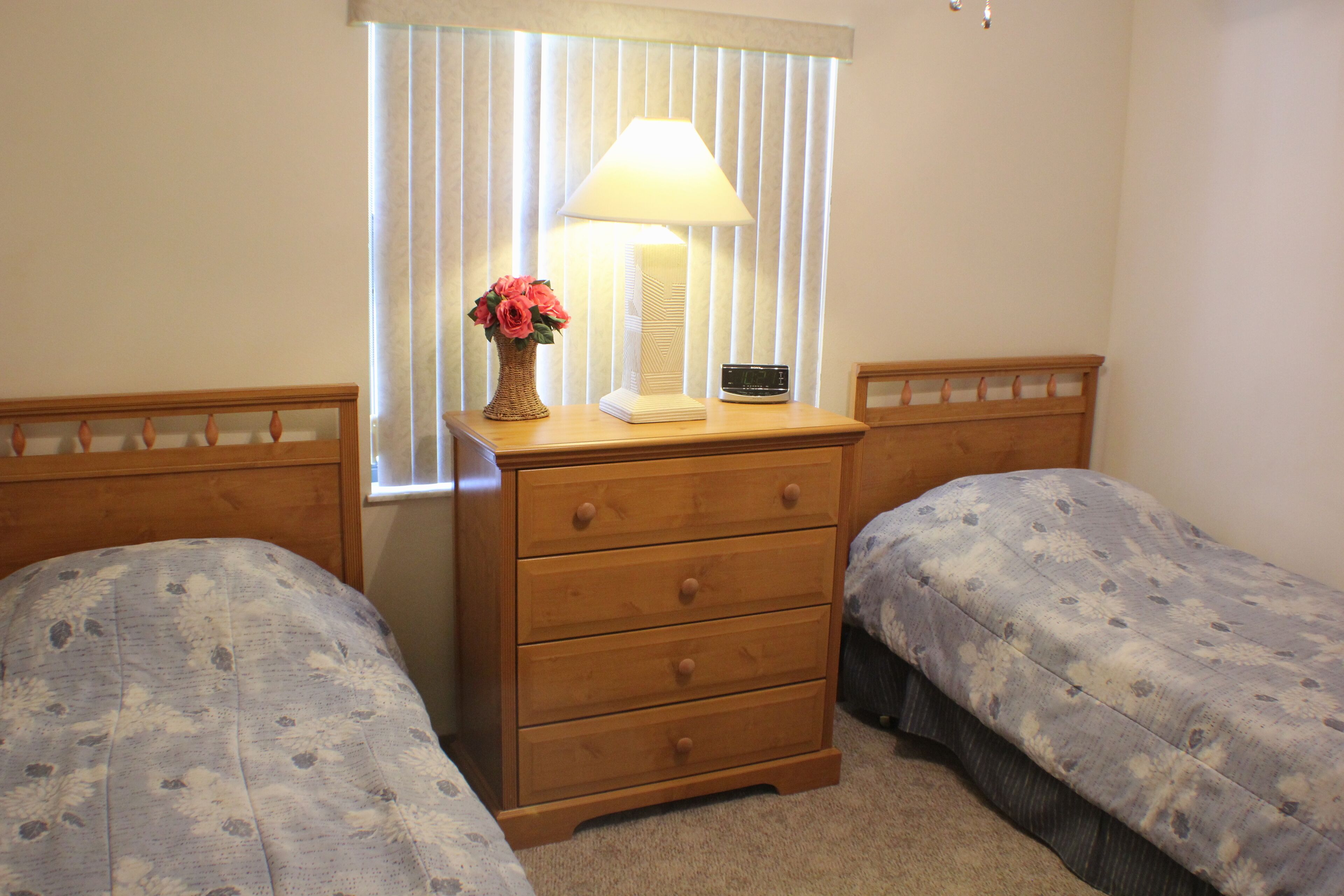 A bedroom with two single beds, a wooden dresser, a lamp, and a radio.