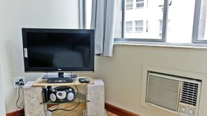 A living room with a flat-screen TV on a stand, a stereo system, and a window with curtains. - Modern Studio by the Beach 103 Apartment 1 (Rio de Janeiro)