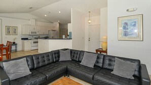 A modern living room with a black leather sectional sofa, a wooden coffee table, and a kitchen in the background. - Villa Grandjean - Comfort - 4 Bedroom (Inverness)