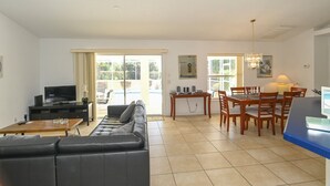 A living room with a sofa, TV, and dining area with chairs and a table. - Villa Grandjean - Comfort - 4 Bedroom (Inverness)