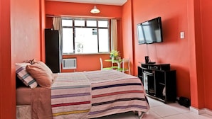 A hotel room with a bed, a TV, a small table with a chair, and a window with curtains. - 8th Floor Ocean View - 101D Holiday home 1 (Rio de Janeiro)