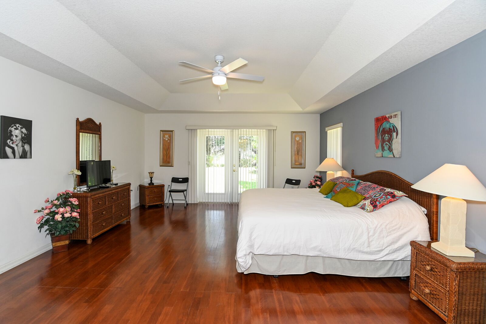 A bedroom with a large bed, a ceiling fan, a dresser, a television, and a chair.