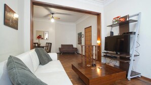 A living room with a white sofa, a wooden coffee table, a TV on a stand, and a ceiling fan. - Wizzie's 3 Bedoom Beach Pad - 304 Apartment 3 (Rio de Janeiro)