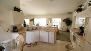 Una cocina compacta con armarios blancos, lavavajillas y un comedor con una silla y una mesa.