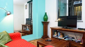Een woonkamer met een rode bank, een houten salontafel, een tv op een houten dressoir en een boekenkast.