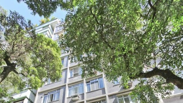 Een meerhoog gebouw met balkons, een hekpoort en omliggend groen.