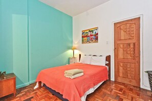 Ein Schlafzimmer mit Bett, Holztür, einem Bild an der Wand und einem Nachttisch mit Lampe.