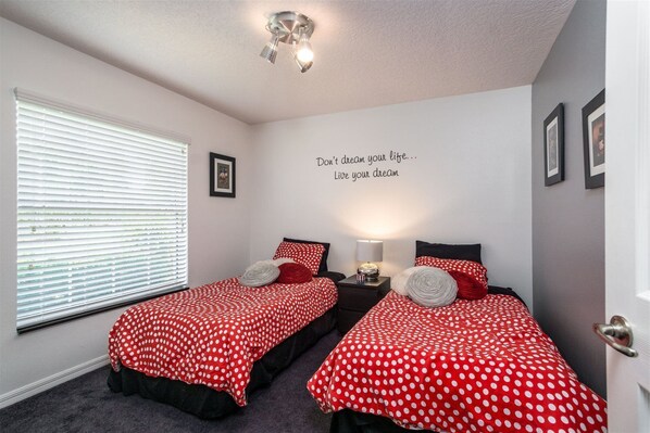 A bedroom with two beds, each with red polka dot bedding, a wall with inspirational text, and a ceiling light fixture. - Villa Ruyper - Executive - 4 Bedroom (Inverness)