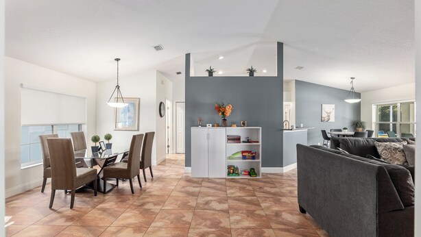 Un salon moderne avec un canapé gris, une table à manger avec des chaises et un coin cuisine doté d’un meuble blanc et d’un petit îlot.