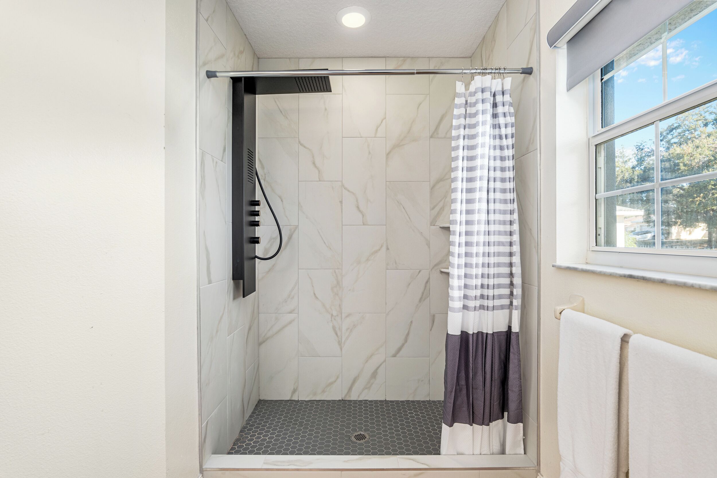 Ducha con puerta de vidrio, barra para toallas y ventana con vistas al exterior.