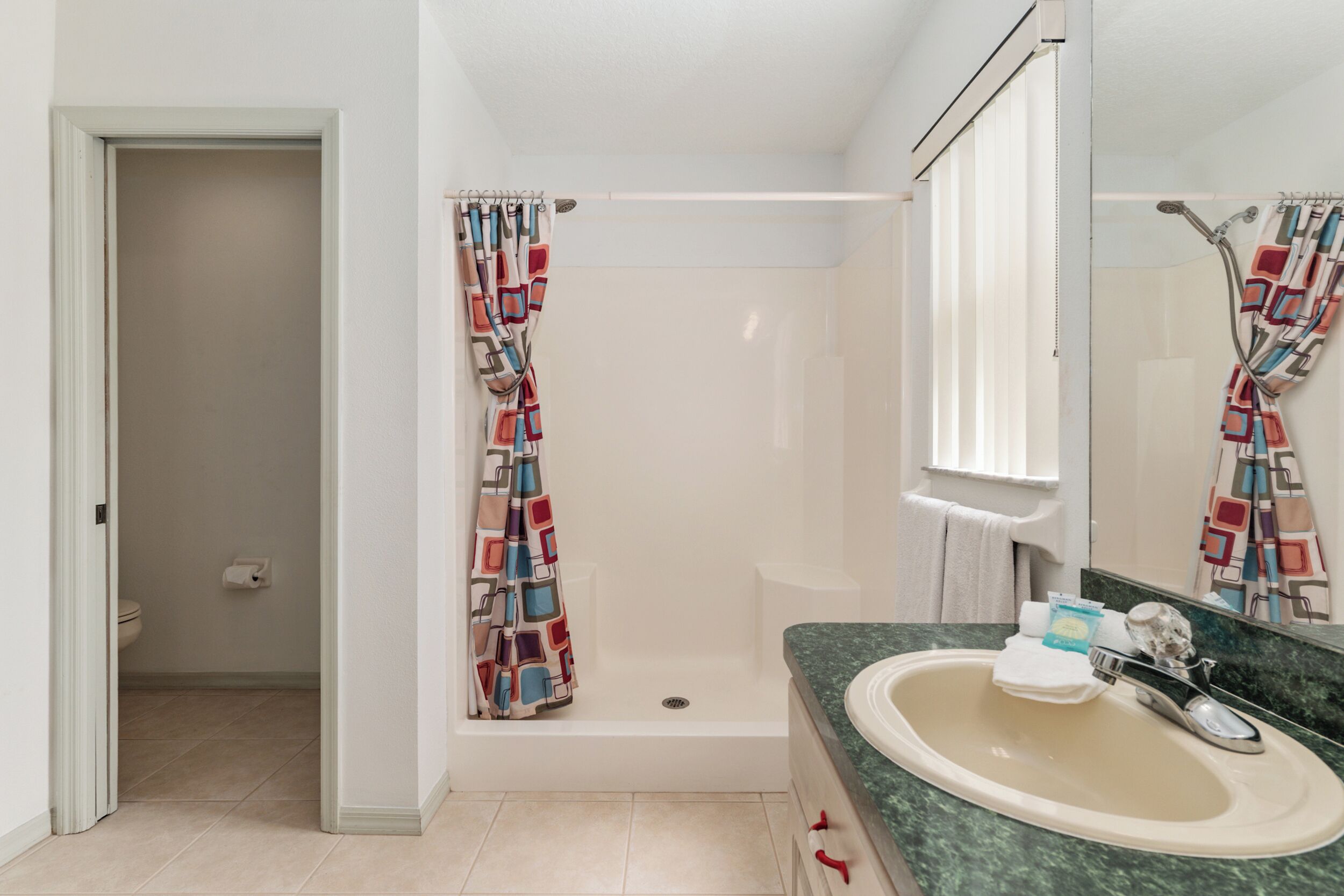 A bathroom with a shower, toilet, sink, and a mirror.