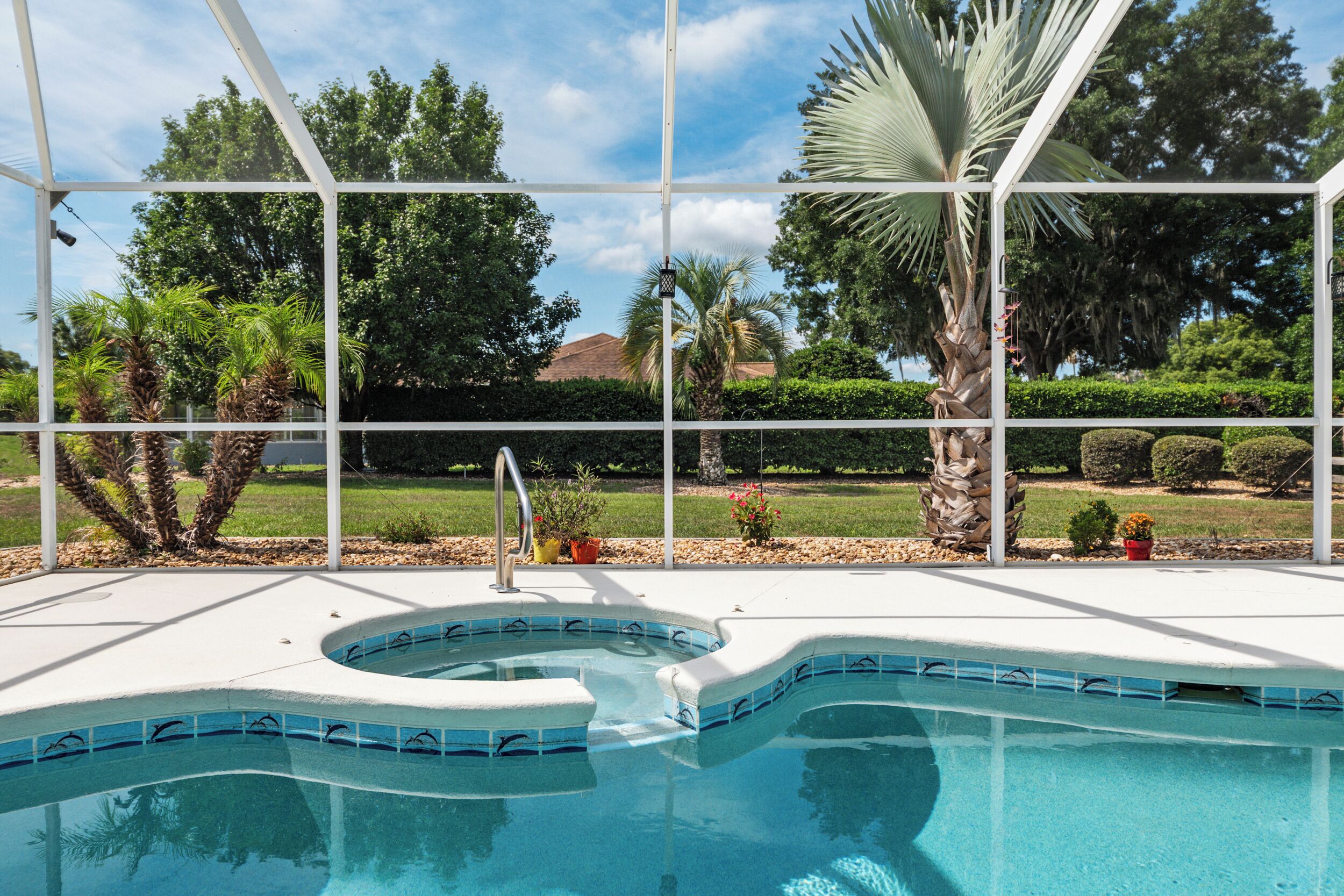 Piscina com design curvo, cercada por um deck branco e uma estrutura de vidro.
